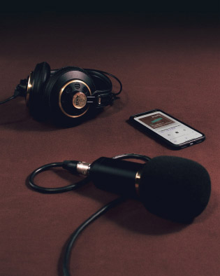 Headphones, microphone, and iPhone with Brownly podcast playing on brown backdrop